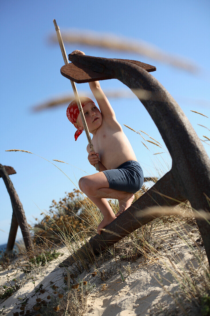 Junge spielt Pirat an einem rostigen Anker am Strand, Ilha de Tavira, Tavira, Algarve, Portugal