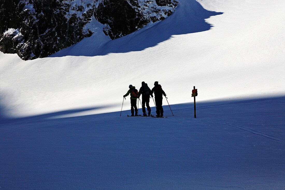 Drei Menschen, Skitouristen steigen mit Skiern auf, vorbei an einem Wegweiser. Die Skitouristen sind unterwegs zum Gipfel des Maljovica im Rila Gebirge, Bulgarien, Europa, MR