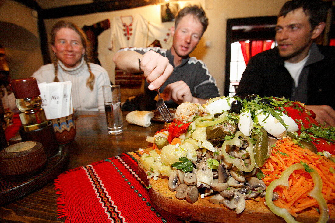 Drei junge Menschen bedienen sich von einer typisch bulgarischen Salatplatte zur Vorspeise in einem Restaurant in Bansko, Pirin Gebirge, Bulgarien, Europa