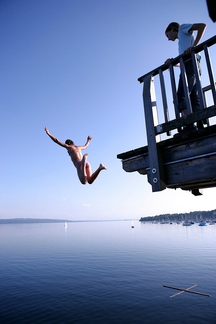 Girl jumping off into the lake from a wooden diving platform, Utting, Ammersee, Bavaria, Germany