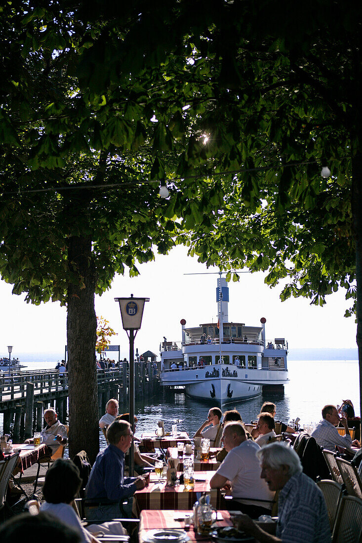 People sitting in a beer garden with steamboat and pier in the background, Herrsching, Ammersee, Bavaria, Germany