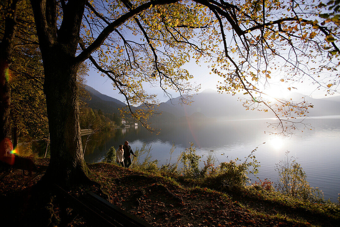 A couple walking along the shore of lake Kochelsee in Autumn, Bavaria, Germany