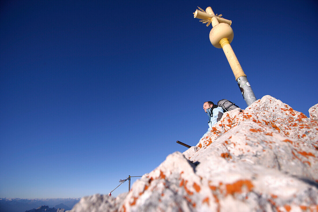 Mann entspannt sich am Gipfelkreuz, Zugspitze, Bayern, Deutschland