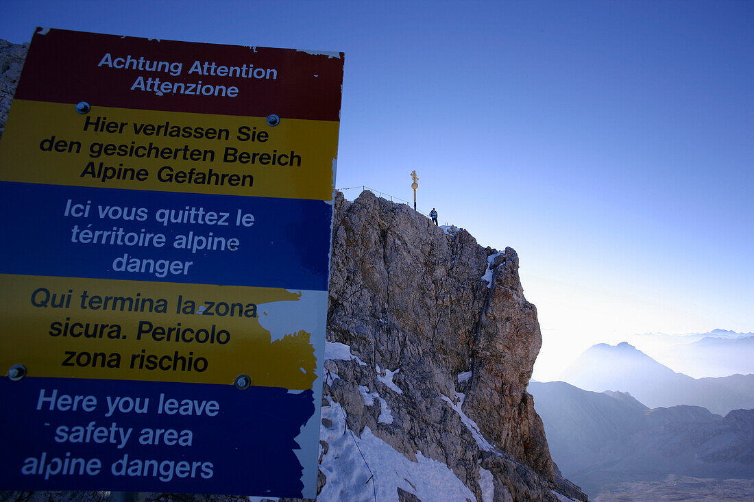 Warning sign and man on summit in the morning light, Zugspitze, Bavaria, Germany
