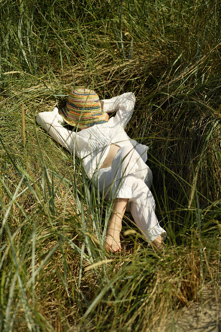 Girl lying on beach grass, hat covering face, Travemuende Bay, Schleswig-Holstein, Germany
