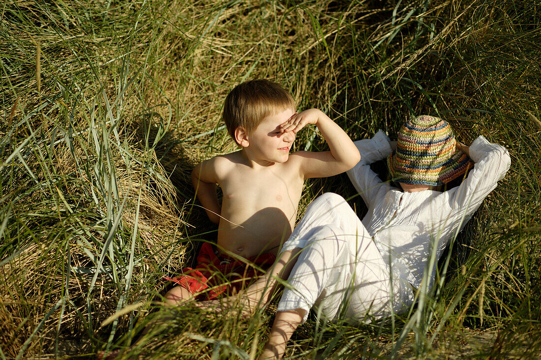 Girl and boy sitting on beach grass, Travemuende Bay, Schleswig-Holstein, Germany