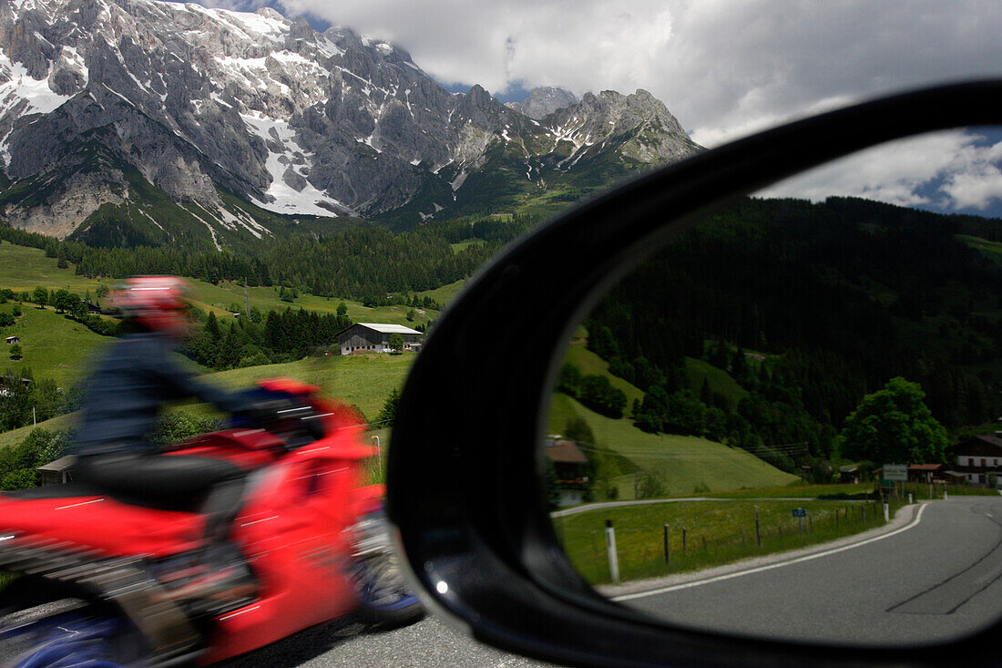 A motorcyclist and view of Dientner Sattel and Hochkonig pass with reflection in car wing mirror, Salzburg, Austria