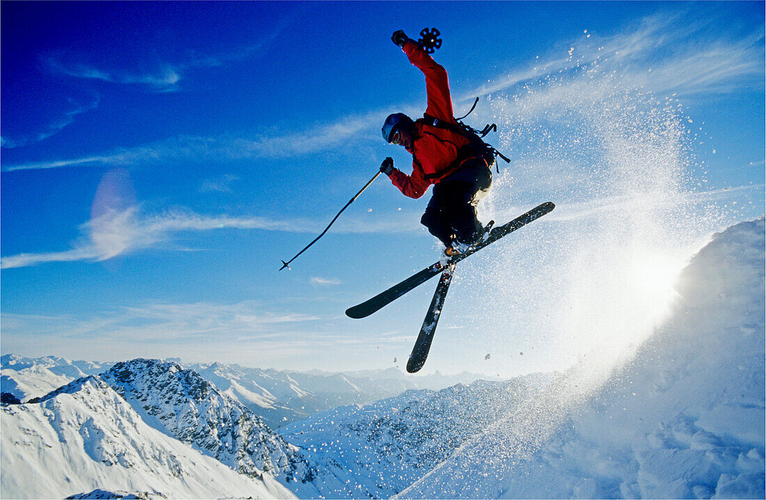 Ein junger Skifahrer, ein Freerider springt mit gekreuzten Skis über eine Schneewächte im Skigebiet Parsenn, Davos, Graubünden, Graubuenden, Schweiz, Alpen, Europa