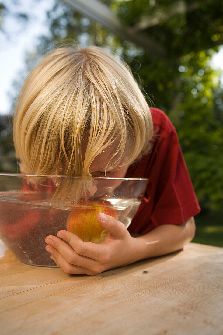 Boy teating an apple in a dish with water, children's birthday party