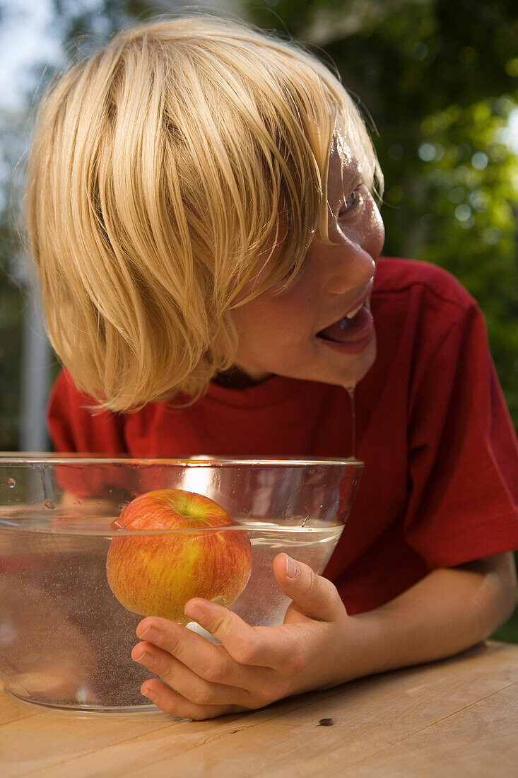 Nasser Junge beugt sich über eine Schüssel mit Wasser und einem Apfel, Kindergeburtstag
