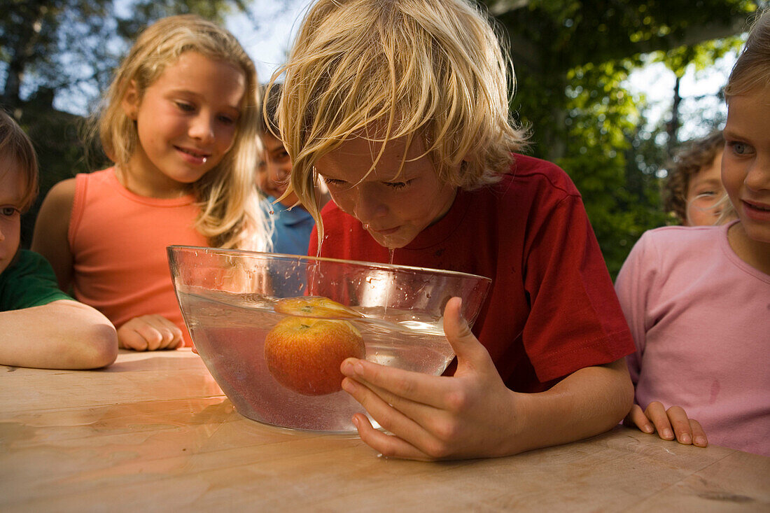 Junge beugt sich über eine Schüssel mit Wasser und einem Apfel, Kindergeburtstag