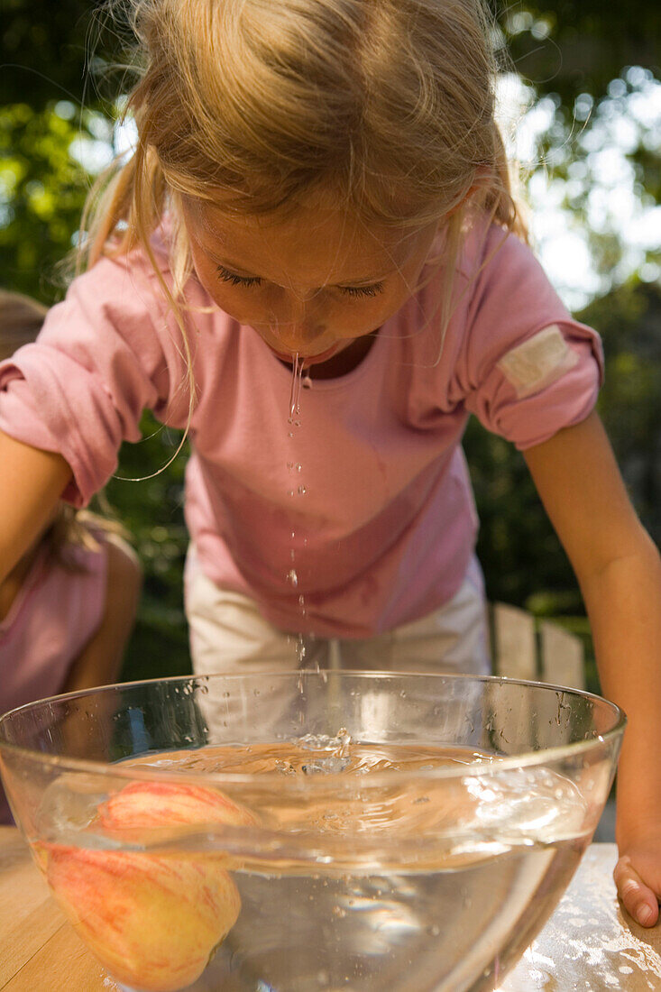 Mädchen beugt sich über eine Schüssel mit Wasser und einen Apfel, Kindergeburtstag