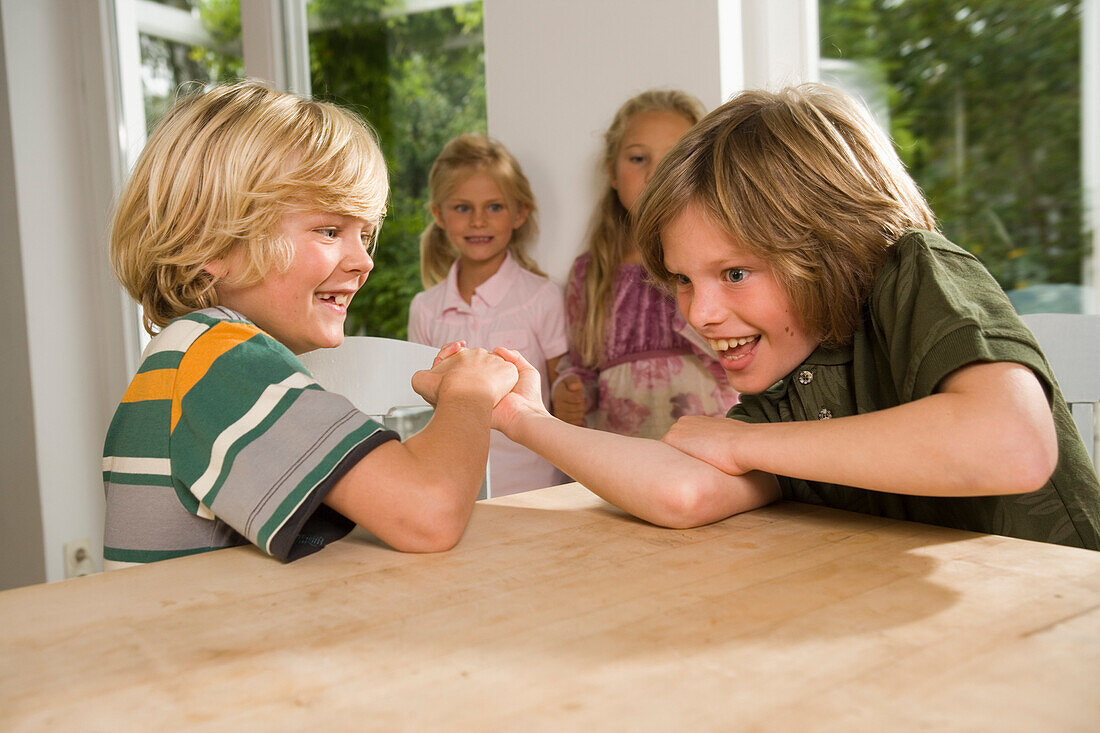 Two boys arm wrestling, girls standing in background, children's birthday party