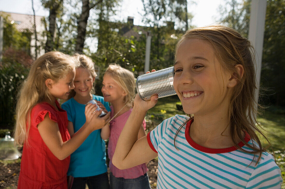 Vier Mädchen spielen mit einem Dosentelefon, Kindergeburtstag
