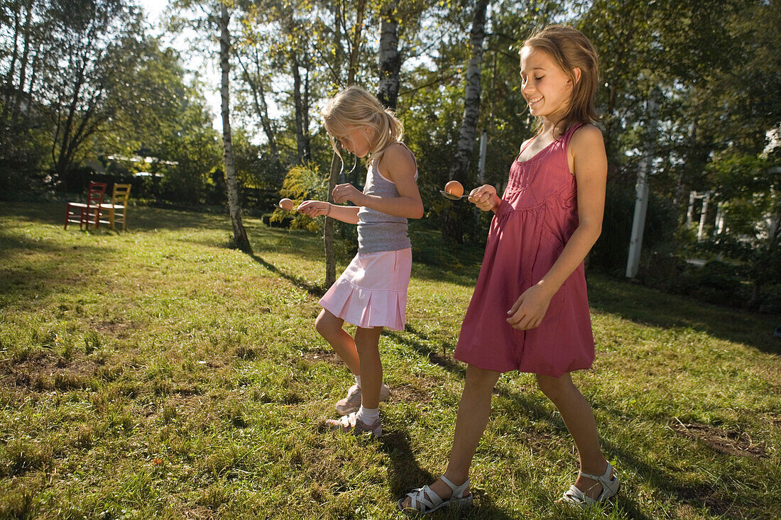 Two girls playing egg-and-spoon race, children's birthday party