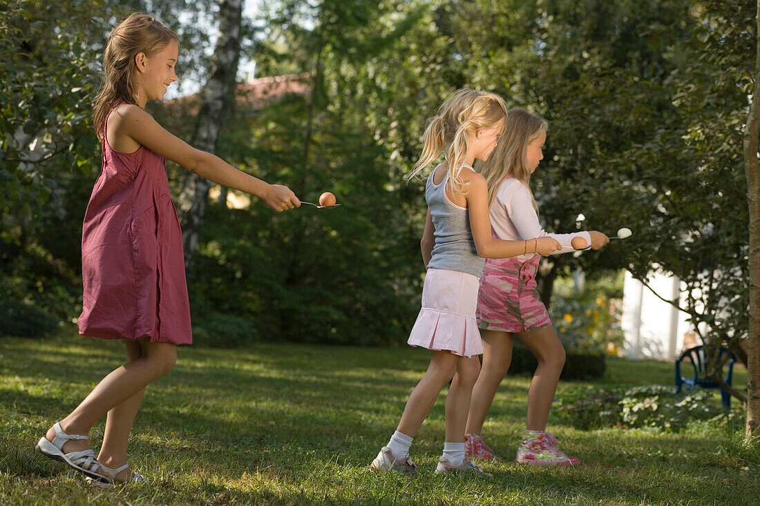 Three girls playing egg-and-spoon race, children's birthday party