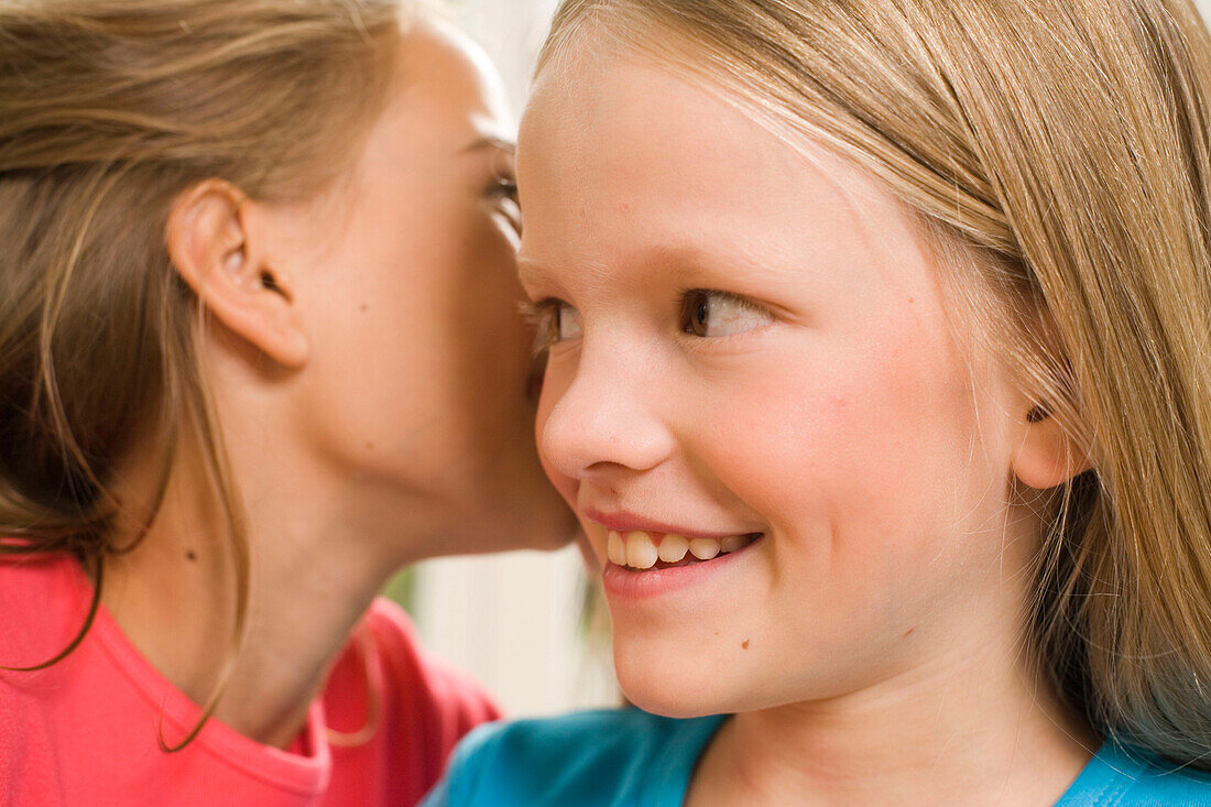 Mädchen flüstert Freundin etwas ins Ohr, Kindergeburtstag