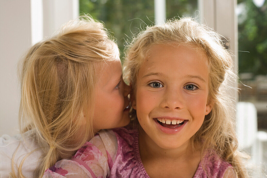 Girl whispering into girlfriend's ear, children's birthday party