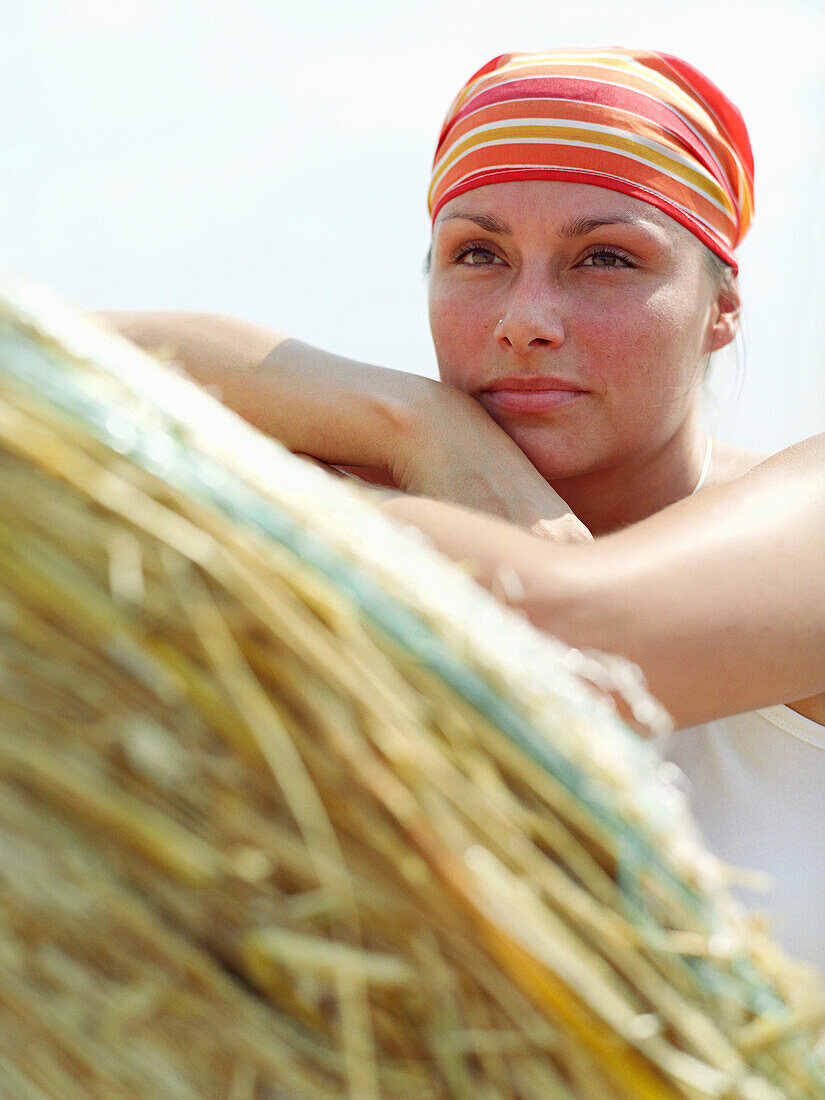 Woman wearing bandanna leaning on a bale of straw looking at view