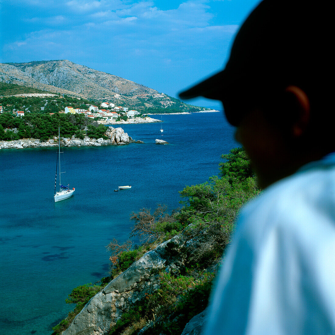 Mann blickt über eine kroatische Küstenlandschaft mit Segelboot, Dalmatien, Kroatien