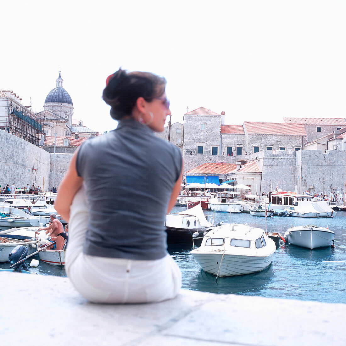 Touristin sitzt am Hafen in der Nähe der Festungsmauer, Dubrovnik, Dalmatien, Kroatien