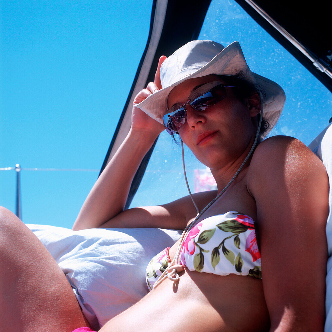 Woman wearing bikini, sunglasses and a hat sitting on sailboat and looking at camera, Dalmatia, Croatia