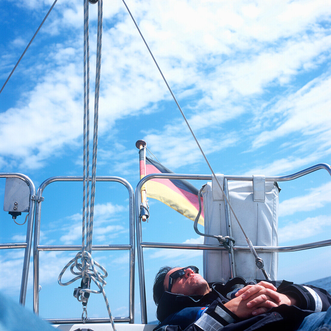 Mann liegt an Deck von einem Segelboot und ruht in der Sonne, Kieler Bucht zwischen Deutschland und Dänemark