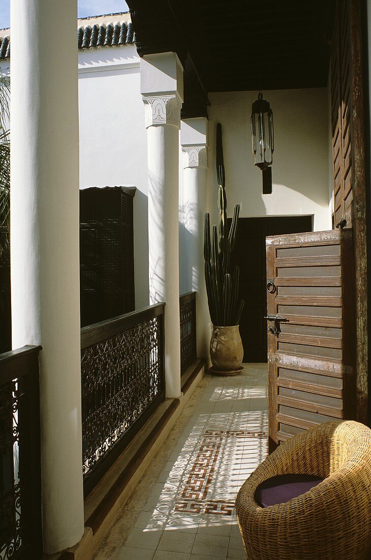 Balkon eines marokkanischen Hauses mit Säulen, Fliesenboden, Korbsessel und Kaktus