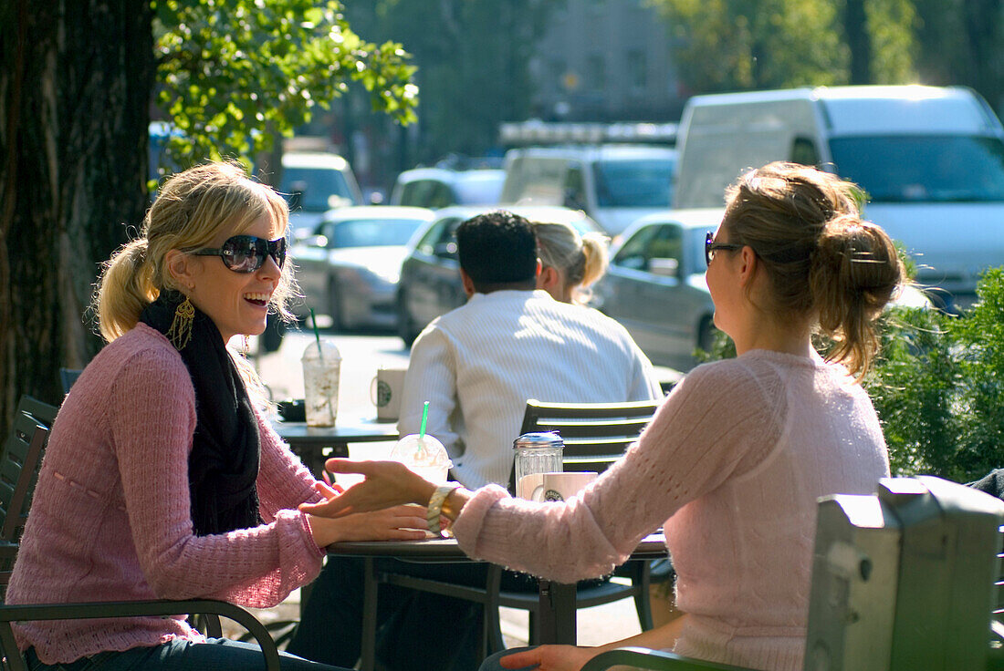 Zwei junge Frauen sitzen in einem Straßencafe, München, Bayern, Deutschland