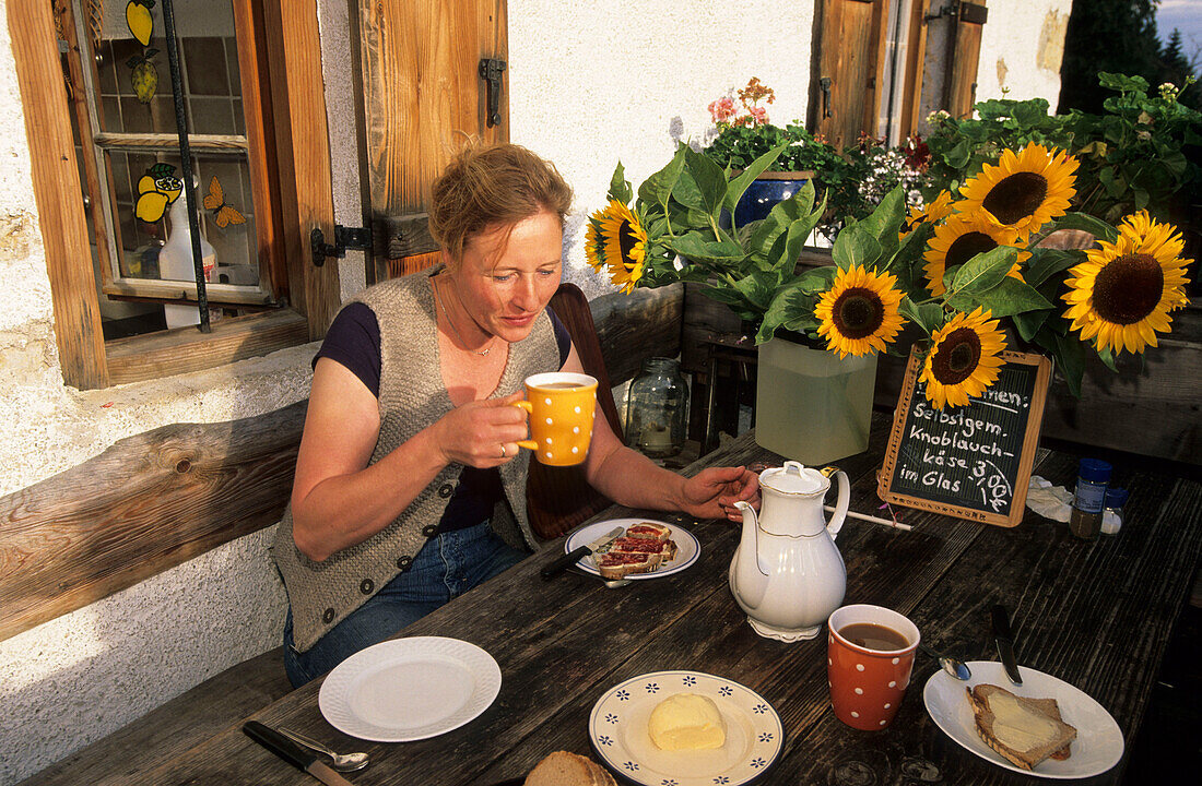 alpine cowgirl having breakfast on the front of the alpine hut, Upper Bavaria, Bavaria, Germany