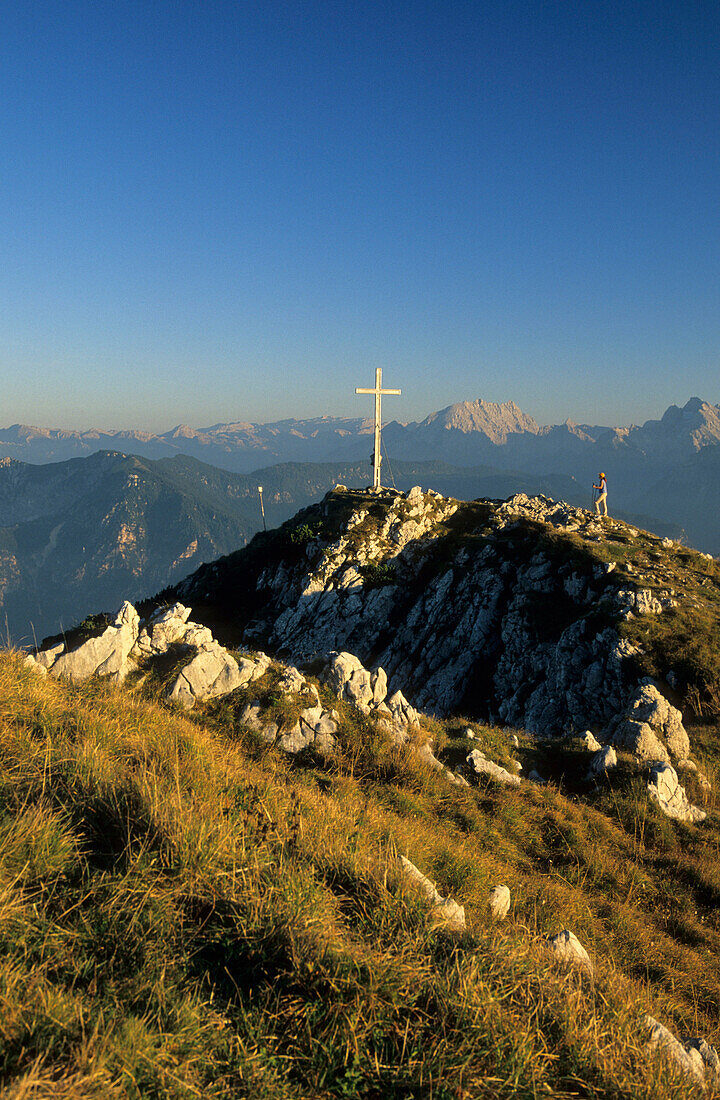 hiker at cross on summit of Zwiesel with view to Berchtesgaden range, Chiemgau, Upper Bavaria, Bavaria, Germany