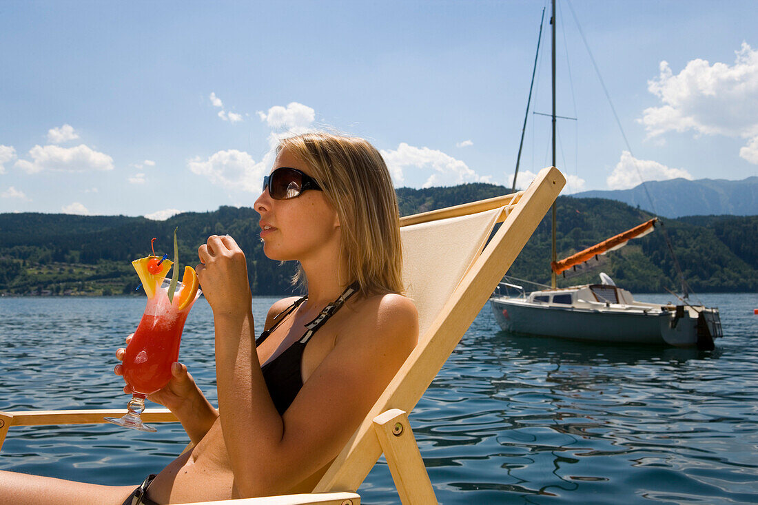 Junge Frau entspannt sich und trinkt einen Fruchtcocktail, Millstätter See, tiefster See Kärntens, Millstatt, Kärnten, Österreich