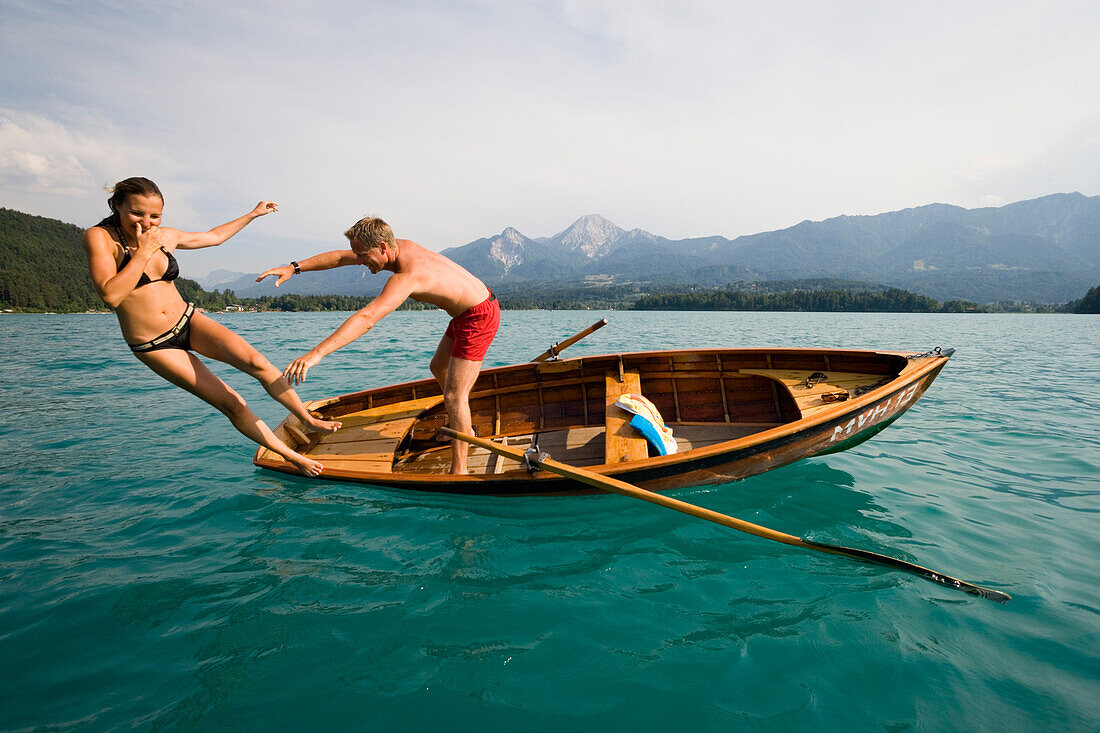 Young man pushes girlfriend from a rowing boat into turquoise water, Lake Faak, Carinthia, Austria