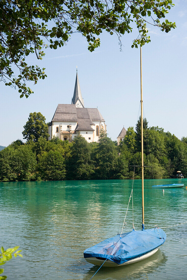 Blick über den Wörthersee, der größte See Kärntens mit ein Segelboot und Maria Wörth mit Kirche im Hintergrund, Kärnten, Österreich