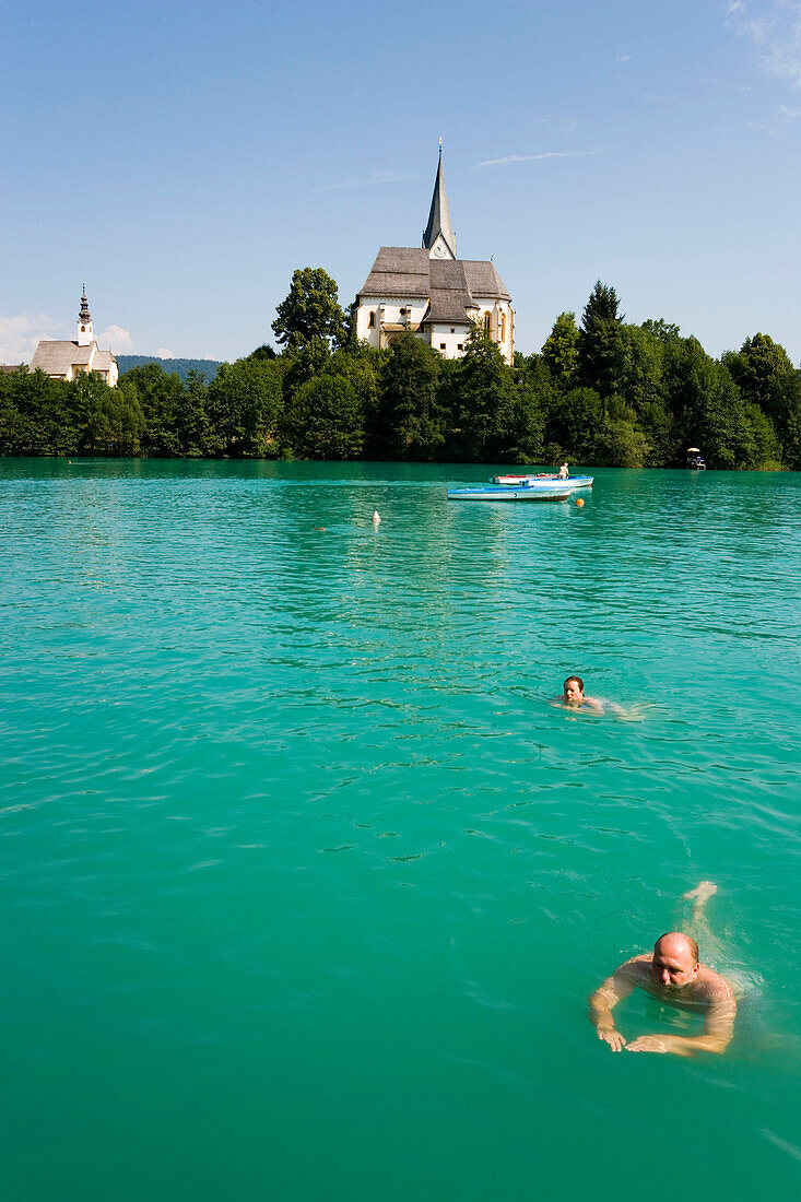 People swimming in the Wörthersee (biggest lake of Carinthia), Parish Church and Rosary Church in background, Maria Wörth, Carinthia, Austria