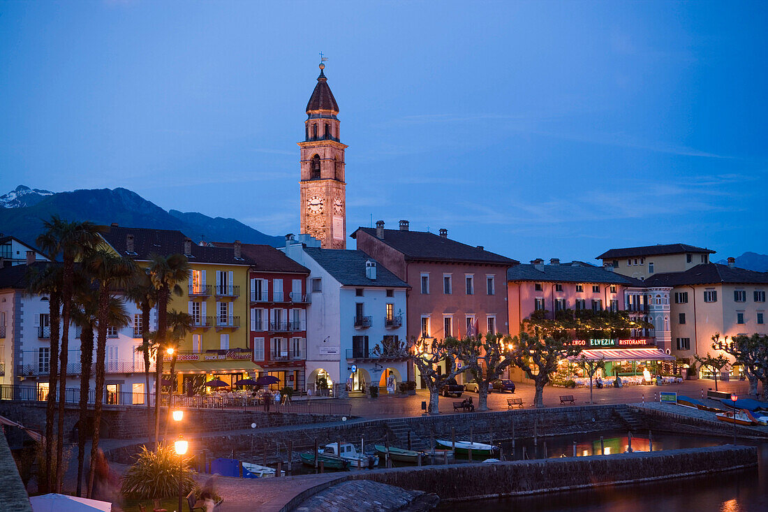 Harbour and harbour promenade with spire of church Santi Pietro Paolo in background in the evening, Ascona, Lake Maggiore, Ticino, Switzerland