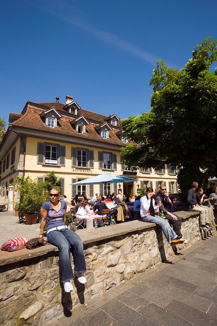 Young people sitting on wall, restaurant in background, Thun (largest garrison town of Switzerland), Bernese Oberland (highlands), Canton of Bern, Switzerland