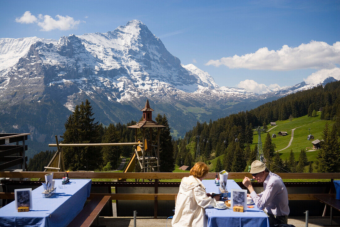 Couple sitting on terrace of the mountain restaurant Berghaus Bort (1600 m), First, Eiger (3970 m) in background, Grindelwald, Bernese Oberland (highlands), Canton of Bern, Switzerland