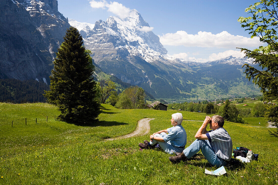 An older couple on the way to Grosse Scheidegg, resting in a meadow and enjoying the view to Eiger 3970 m and Schreckhorn 4078 m, Grindelwald, Bernese Oberland, Canton of Bern, Switzerland