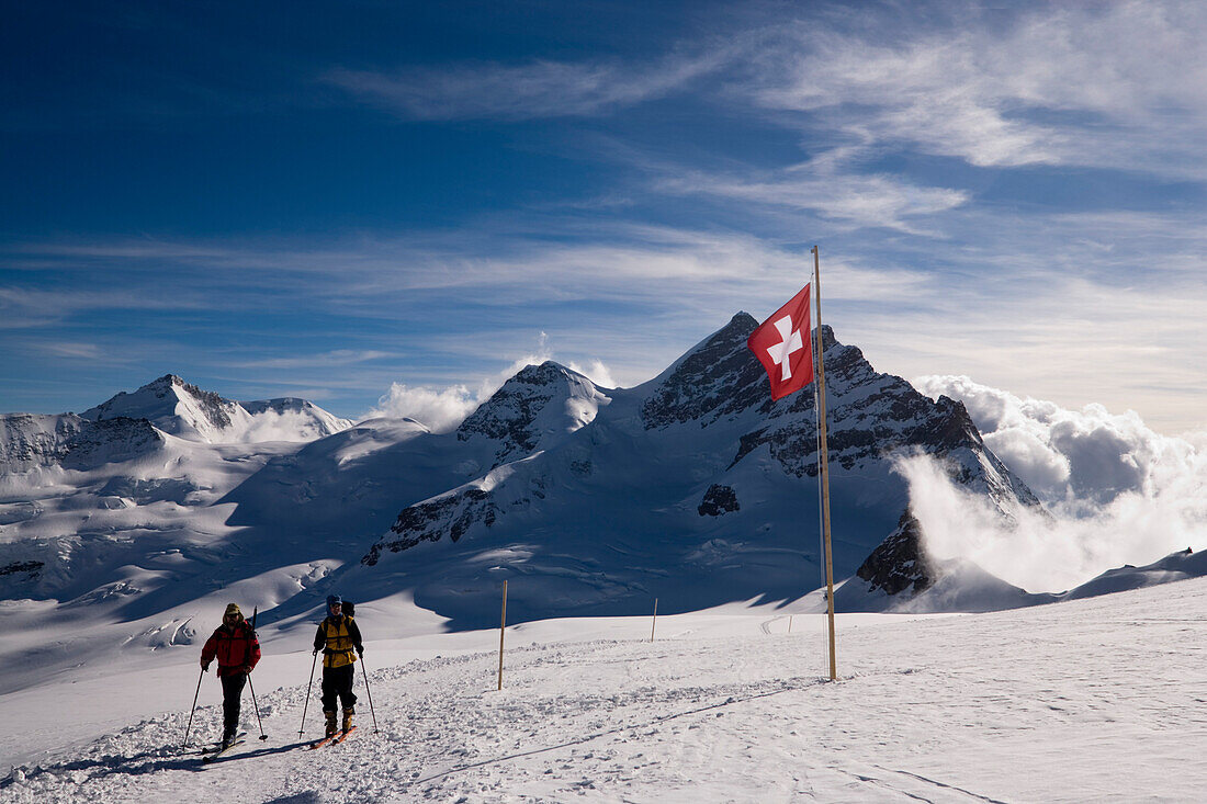 Two people hiking at Jungfraufirn glacier, passing a Swiss flag, Grindelwald, Bernese Oberland, Canton of Bern, Switzerland