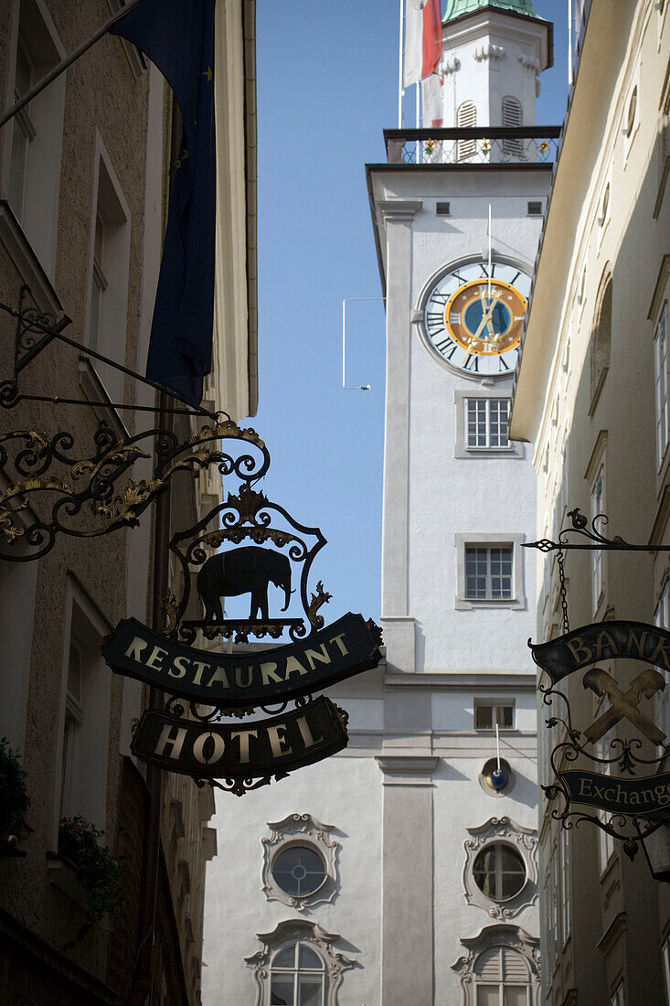 Wrought-iron shop sign at a house wall, city hall tower in background, Getreidegasse, Salzburg, Salzburg, Austria, Since 1996 historic centre of the city part of the UNESCO World Heritage Site