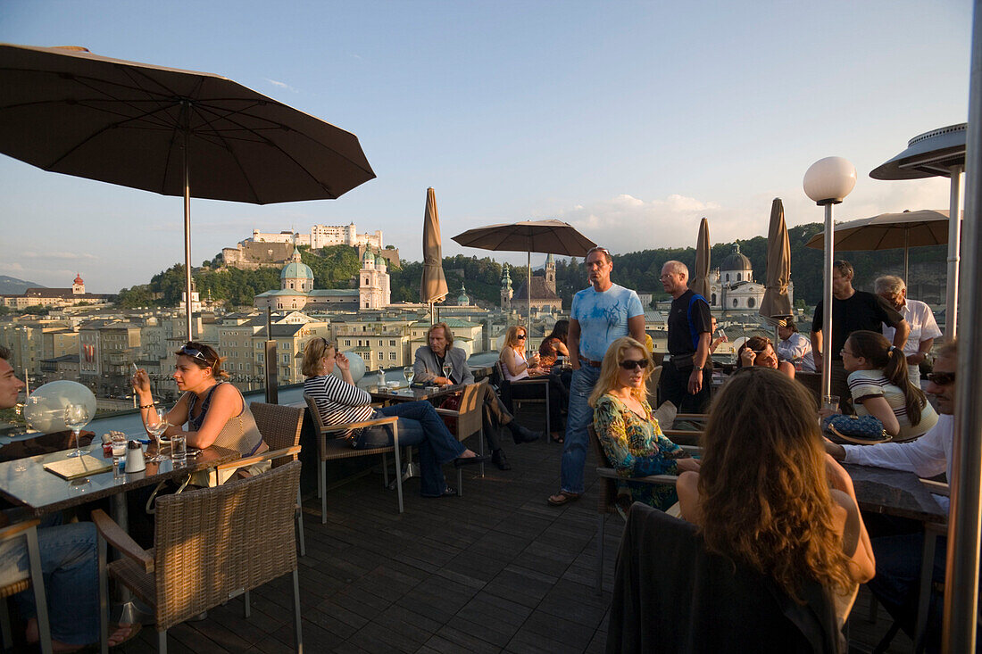 Guests sitting on roof deck of restaurant Hotel Stein, panoramic view over old town with Salzburg Cathedral, Franciscan Church, Collegiate Church, built by Johann Bernhard Fischer von Erlach, and Hohensalzburg Fortress, largest, fully-preserved fortress i