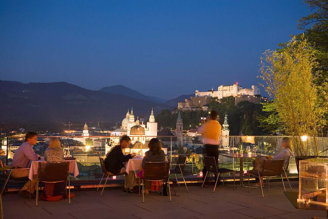 People sitting on terrace of the restaurant Mönchsberg 32 in the evening, view over old town with Hohensalzburg Fortress, Salzburg, Salzburg, Austria, Since 1996 historic centre of the city part of the UNESCO World Heritage Site