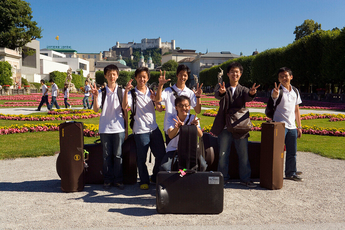Members of the Asian Youth Orchestra smiling at camera, Mirabell castle and garden, Hohensalzburg Fortress, largest, fully-preserved fortress in central Europe, in background, Salzburg, Salzburg, Austria