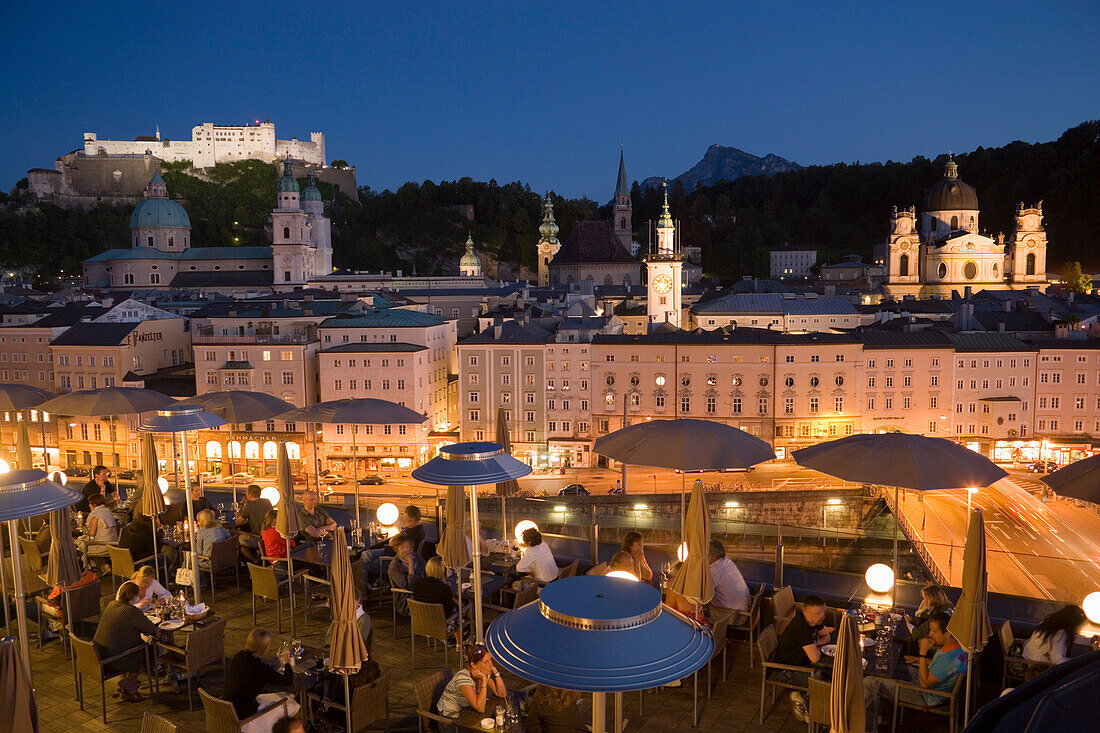 View over the illuminated roof terrace of restaurant Hotel Stein in the evening, to old town with Salzburg Cathedral, St. Peter's Archabbey, Franciscan Church and Hohensalzburg Fortress the largest fully preserved fortress in central Europe, Salzburg, Sal