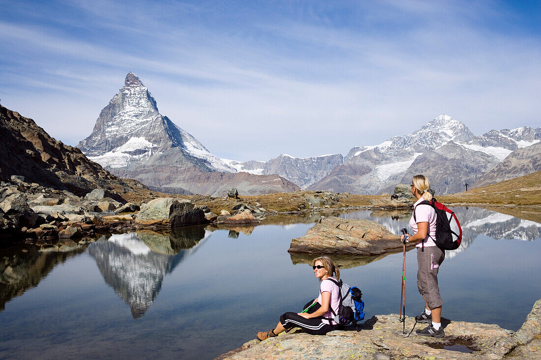 Two female hikers looking at the reflection of the east face, Hoernligrat, of the Matterhorn, 4478 m, in Riffelsee, Zermatt, Valais, Switzerland