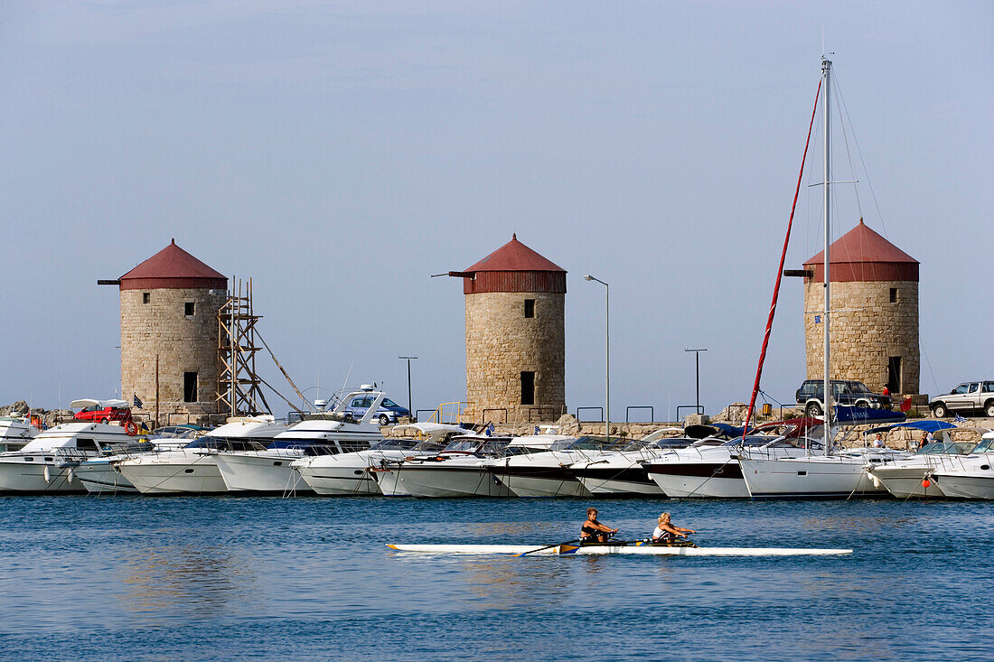 Women rowing in the Mandraki harbour (translated literally: fold), anchoring ships and  windmills on mole in background, Rhodes Town, Rhodes, Greece
