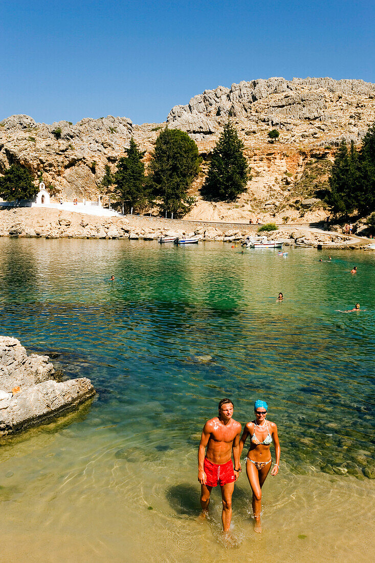 Couple walking through water of the Saint Paul's Bay (Agios Pavlos), Lindos, Rhodes, Greece
