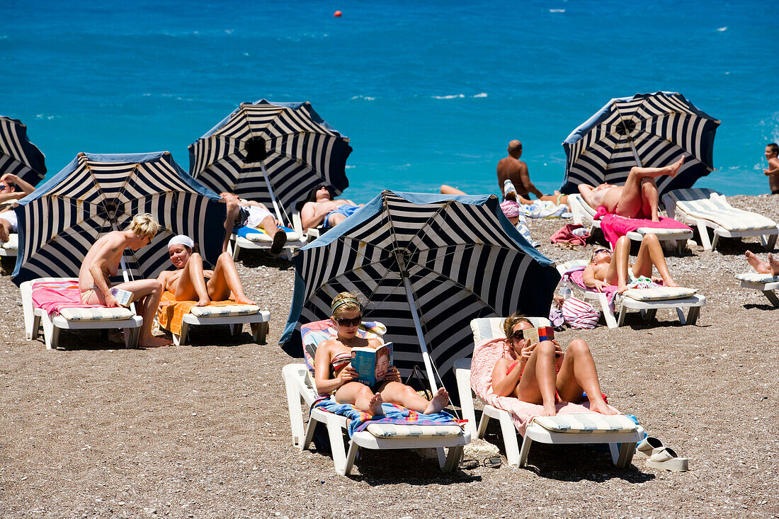 People sunbathing on sunloungers at main beach, Rhodes Town, Rhodes, Greece
