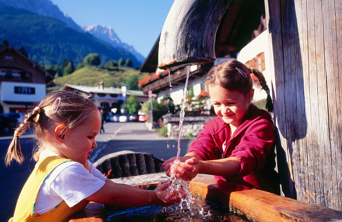 Two children playing at a fountain, Grainau, Upper Bavaria, Bavaria, Germany, Europe